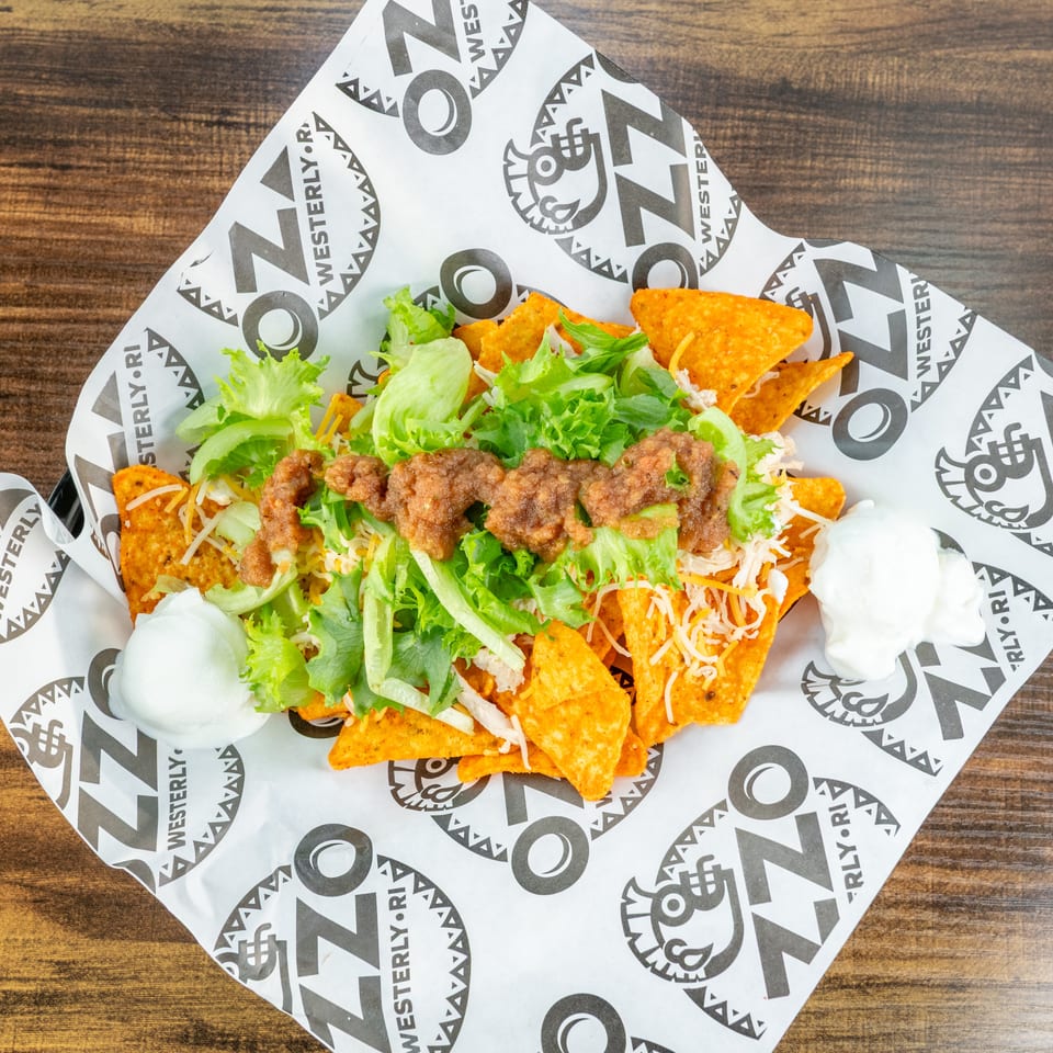 Loaded nachos topped with seasoned beef, shredded cheese, lettuce, chicken, and sour cream on branded paper.