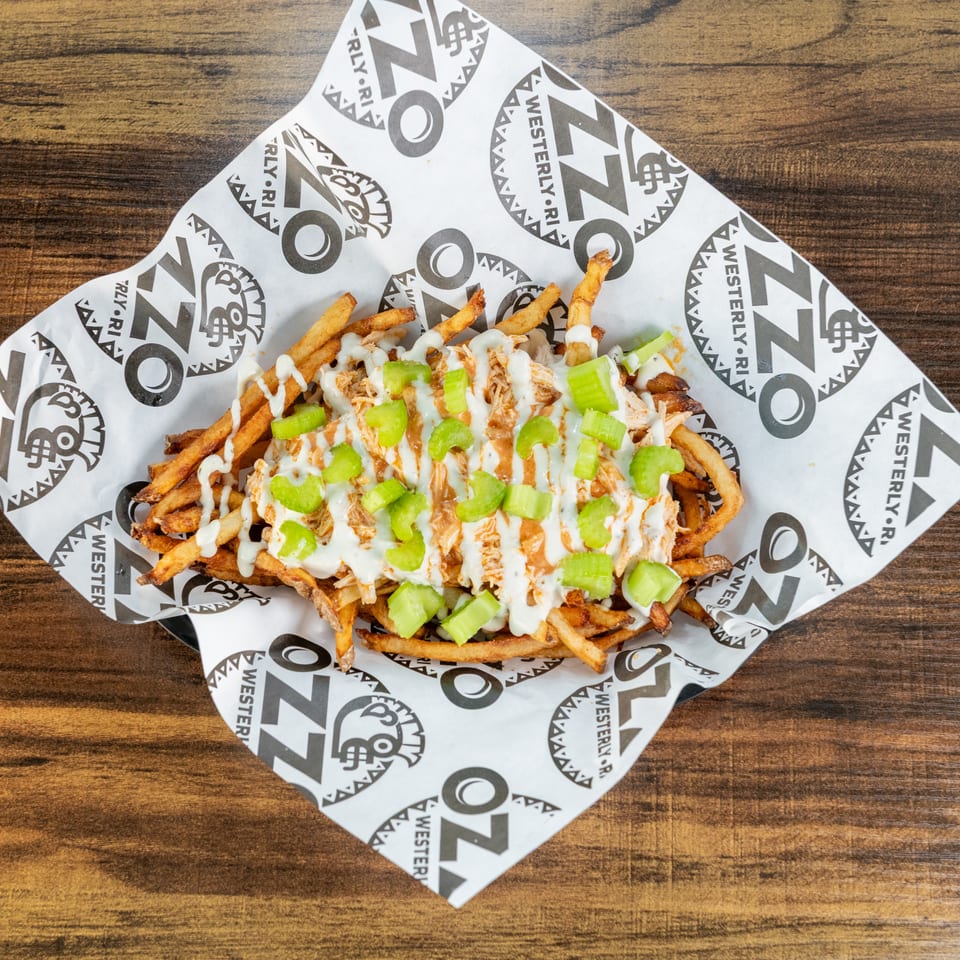 Loaded fries topped with shredded chicken, creamy sauce, hot sauce, and chopped celery on branded paper.