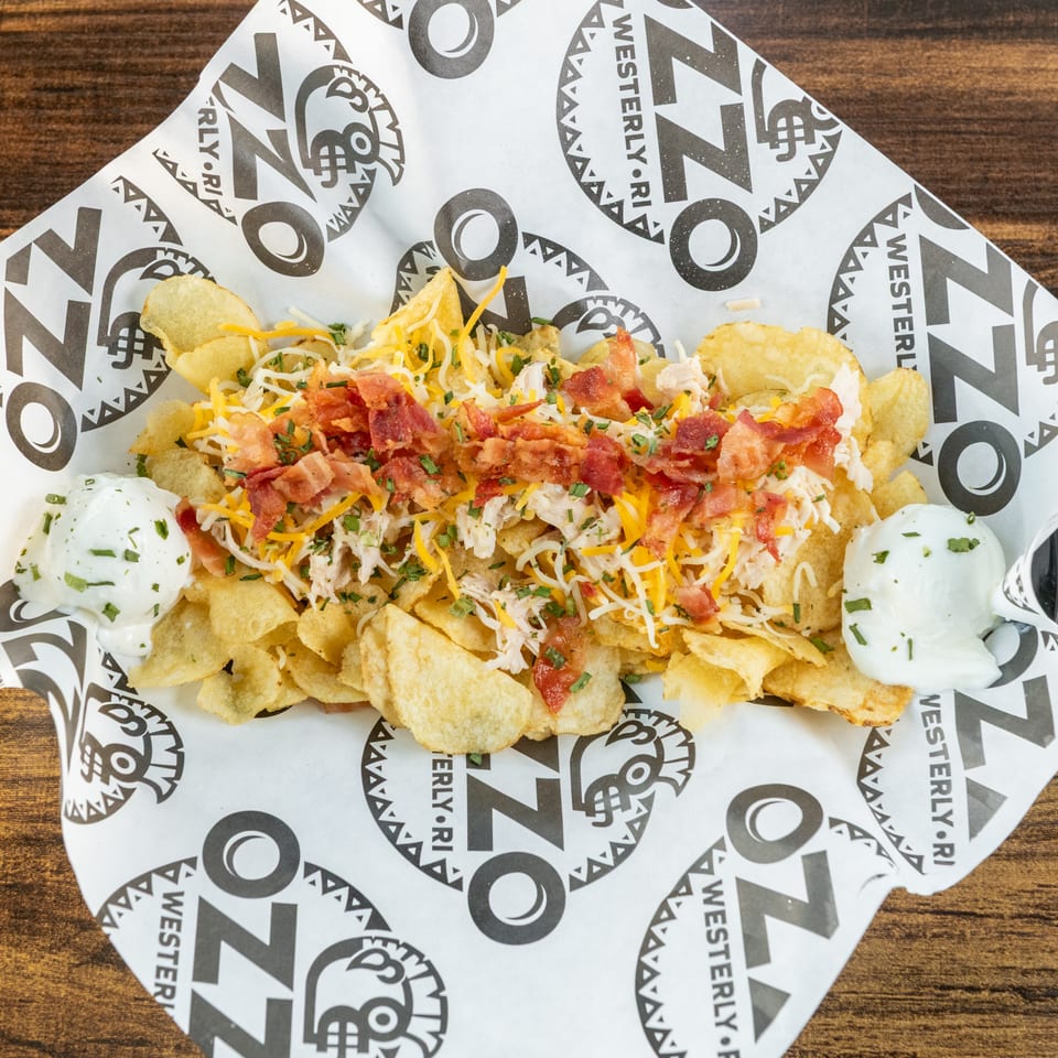 Loaded nachos topped with shredded chicken, cheese, bacon, herbs, salsa, and sour cream on branded paper.