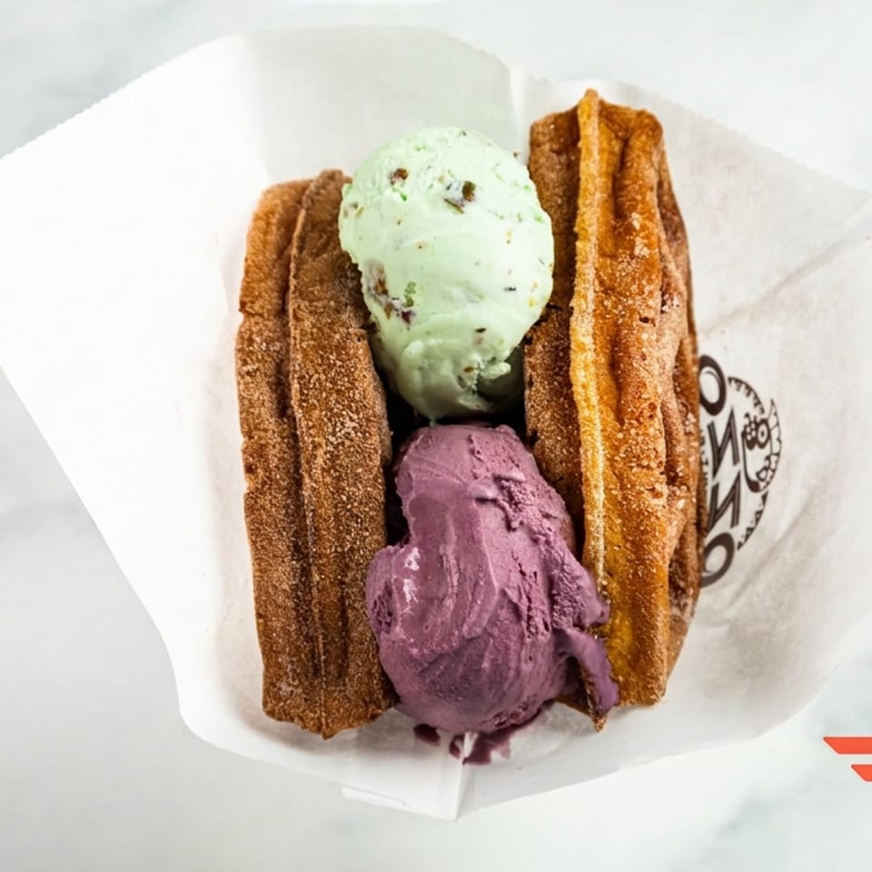 Crispy churro waffle sandwich filled with mint chocolate chip and purple ice cream, served in branded paper.