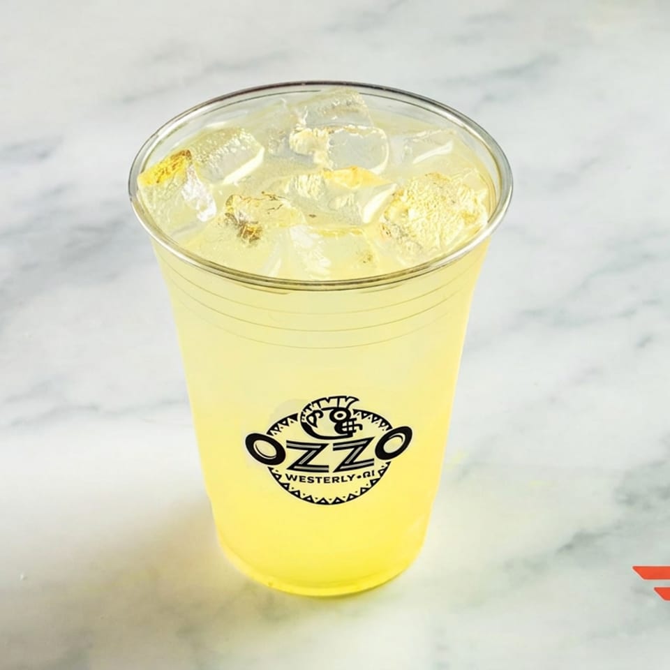 Plastic cup of iced yellow lemonade bearing the Ozzo restaurant logo on a marble tabletop.